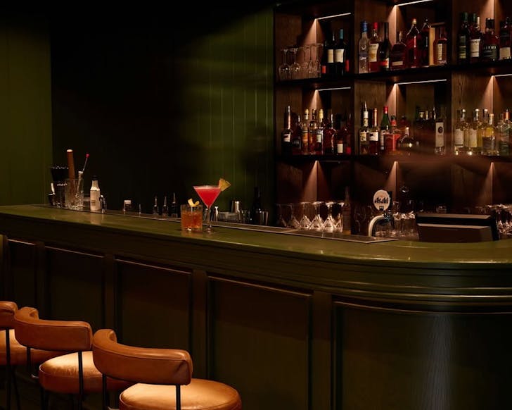 Two cocktails sit atop a moody bar counter. 