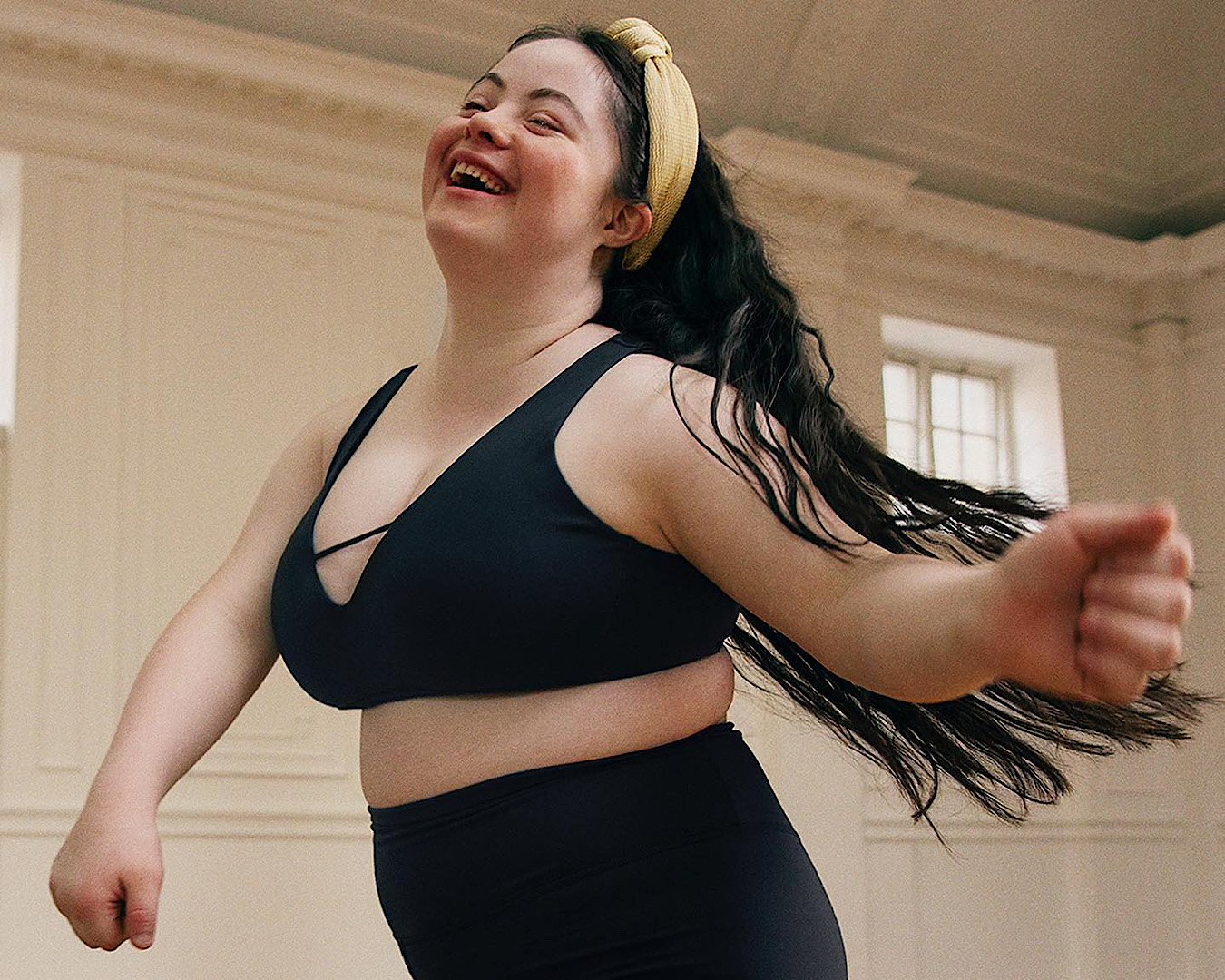 A woman wearing a matching set of black Adidas leggings and bra is loving life as she spins around the room. 