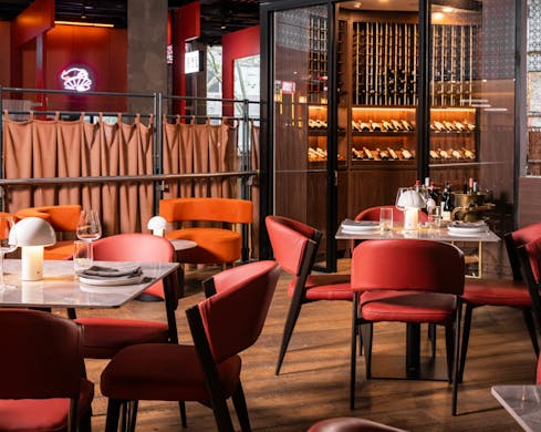 An indoor dining area without any people, featuring wooden floorboards, plush red chairs and a bar in the background.