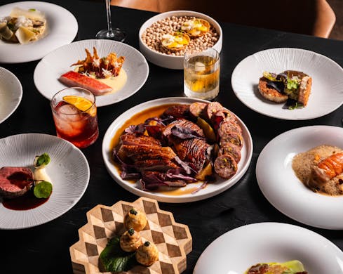 Above view of various dishes served on the table, including juicy meats, delicate servings of marron udon, and a couple of drinks amongst the plates.