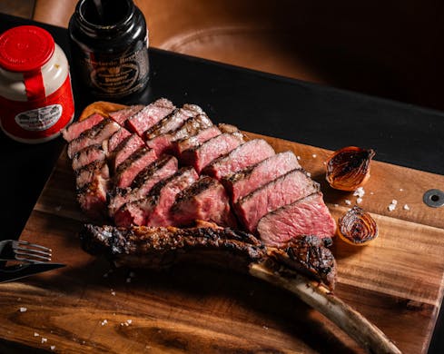 A birds-eye view of tender Wagyu tomahawk on a wooden board. The meat is sliced to reveal the rare, juicy inside. 