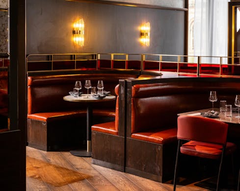Indoor booth seating at the restaurant. The booths are a deep red and there is low-lit lamps creating a romantic mood.