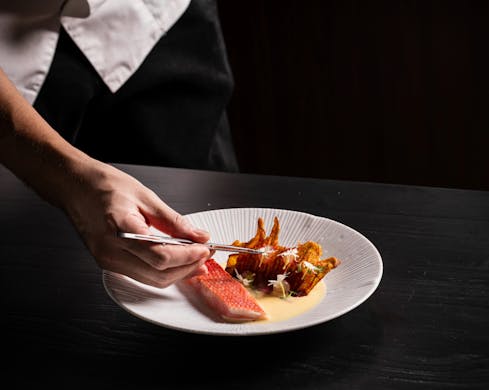 A chef's hand adding the final touches to a dish of seafood.