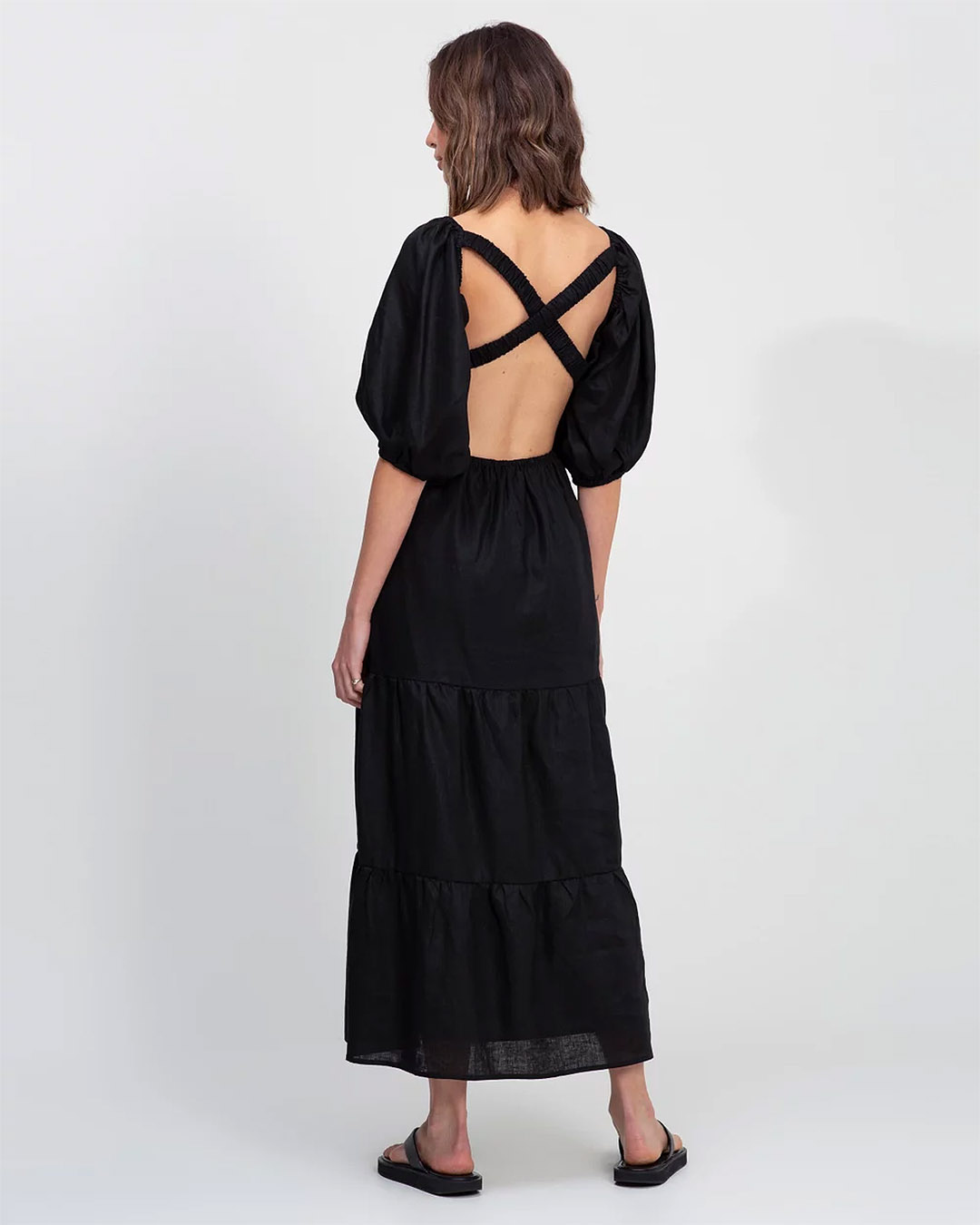 We see the back of a woman’s black dress with balloon sleeves and crossed straps over a back cutout. 