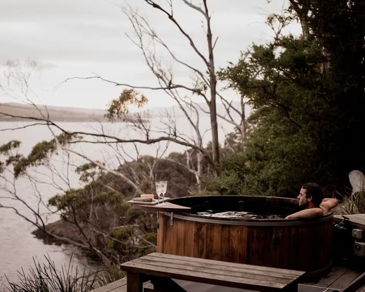 A man sits in the hot tub looking out to Bruny Island at Aerie Retreat lake house Airbnb one of the best in Tasmania
