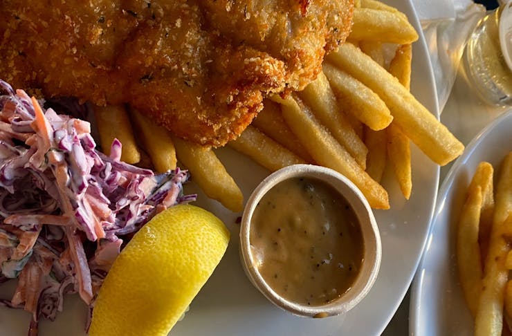 A golden chicken scnitzel with slaw and chips.