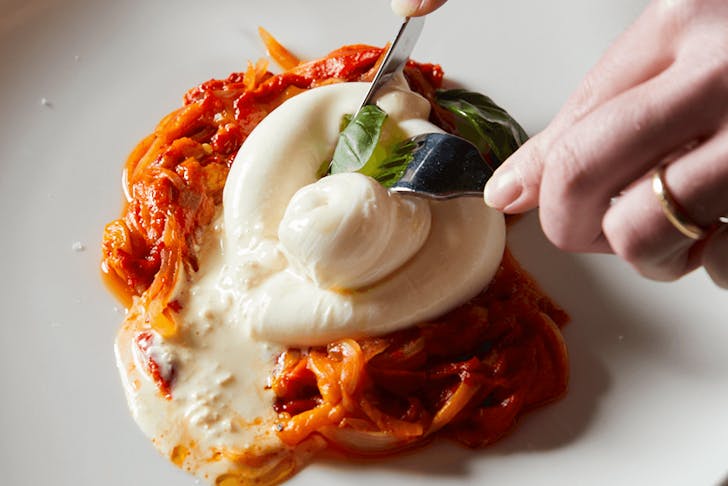 A thick burrata on roasted peppers with a person cutting into it. 