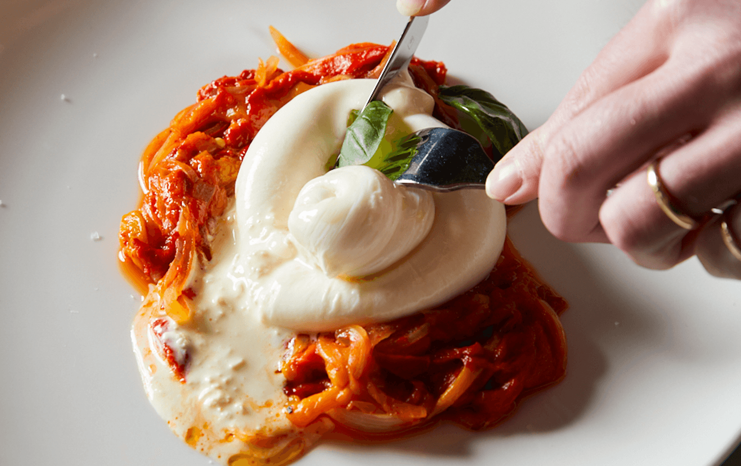 A thick burrata on roasted peppers with a person cutting into it. 