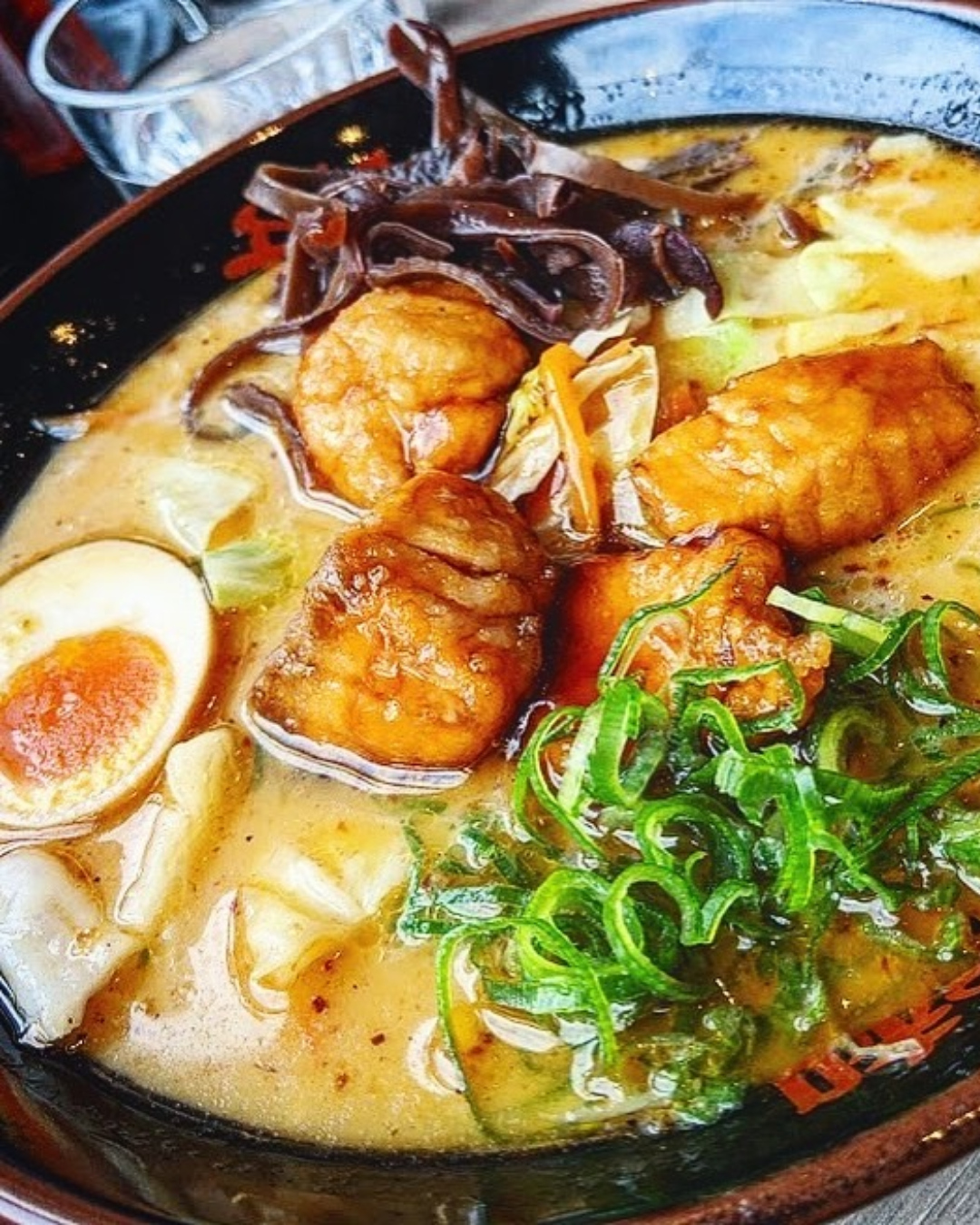A bowl of ramen featuring huge chunks of salmon in a rich, vibrant-couloured broth. 