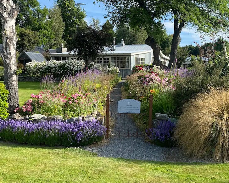 A gate and path, bordered by wildflowers, which leads to Aldourie Lodge, one of the best places to stay in Lake Tekapo. 