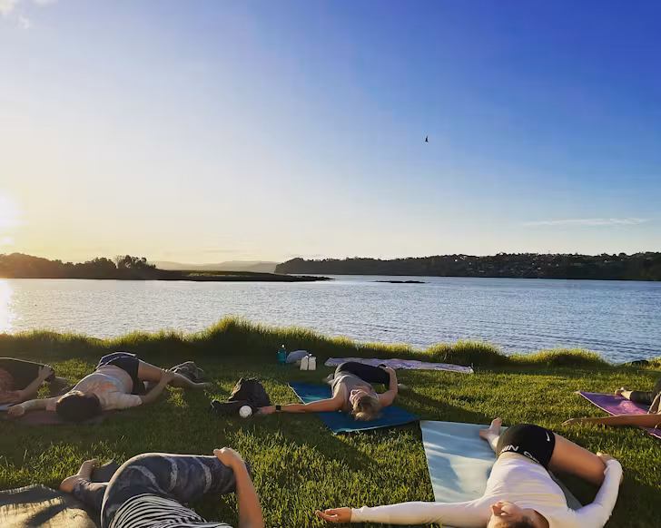 Yogis lie on their mats on the grass with a sea view at Ambury Farm at a Being yoga event. 