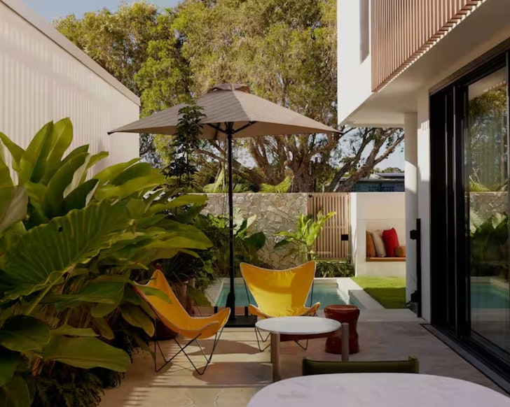 Yellow chairs beneath an umbrella by the pool at Ammamead House one of the best Byron Bay Airbnbs