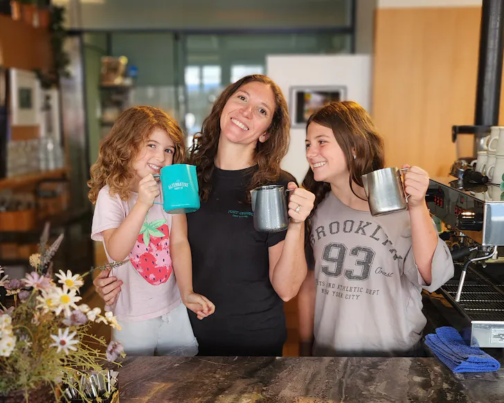 Andrea and her two kids hold milk jugs and stand at the counter of Fort Greene.