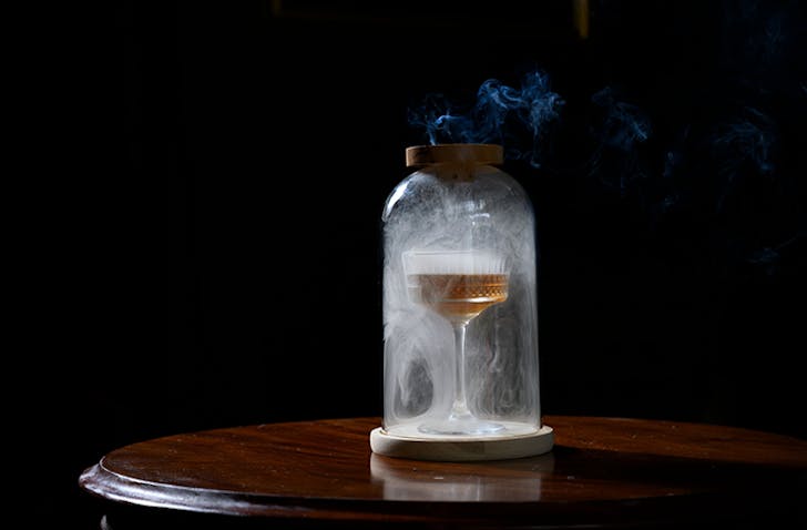 A closh sits on top of a cocktail with smoke filling the closh, at one of the best cocktail bars Melbourne has to offer called Antique Bar