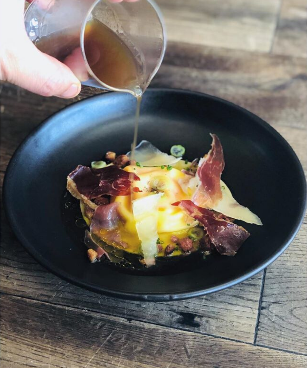 Bone broth poured over raviolo of agria and egg yolk with iberico consommé and brioche crouton.