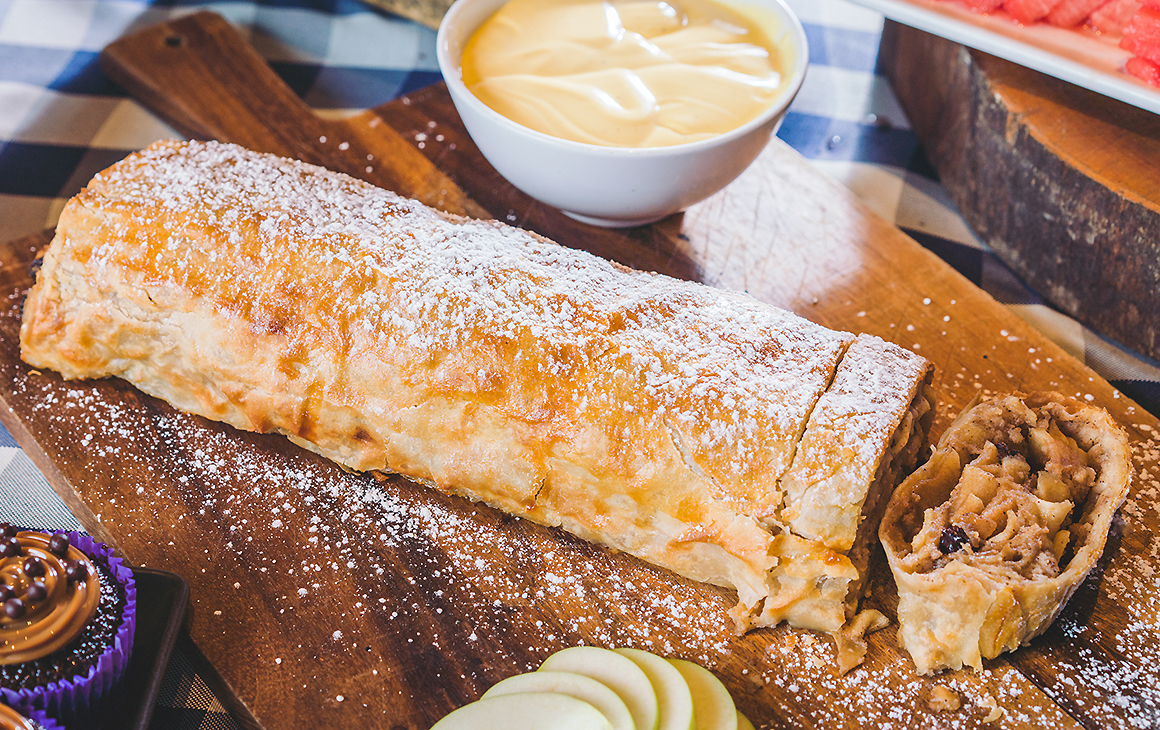 Apple Strudel from The Bavarian sits looking impressive on a long board with apple and creme Anglaise nearby, one of the best winter desserts in Auckland.
