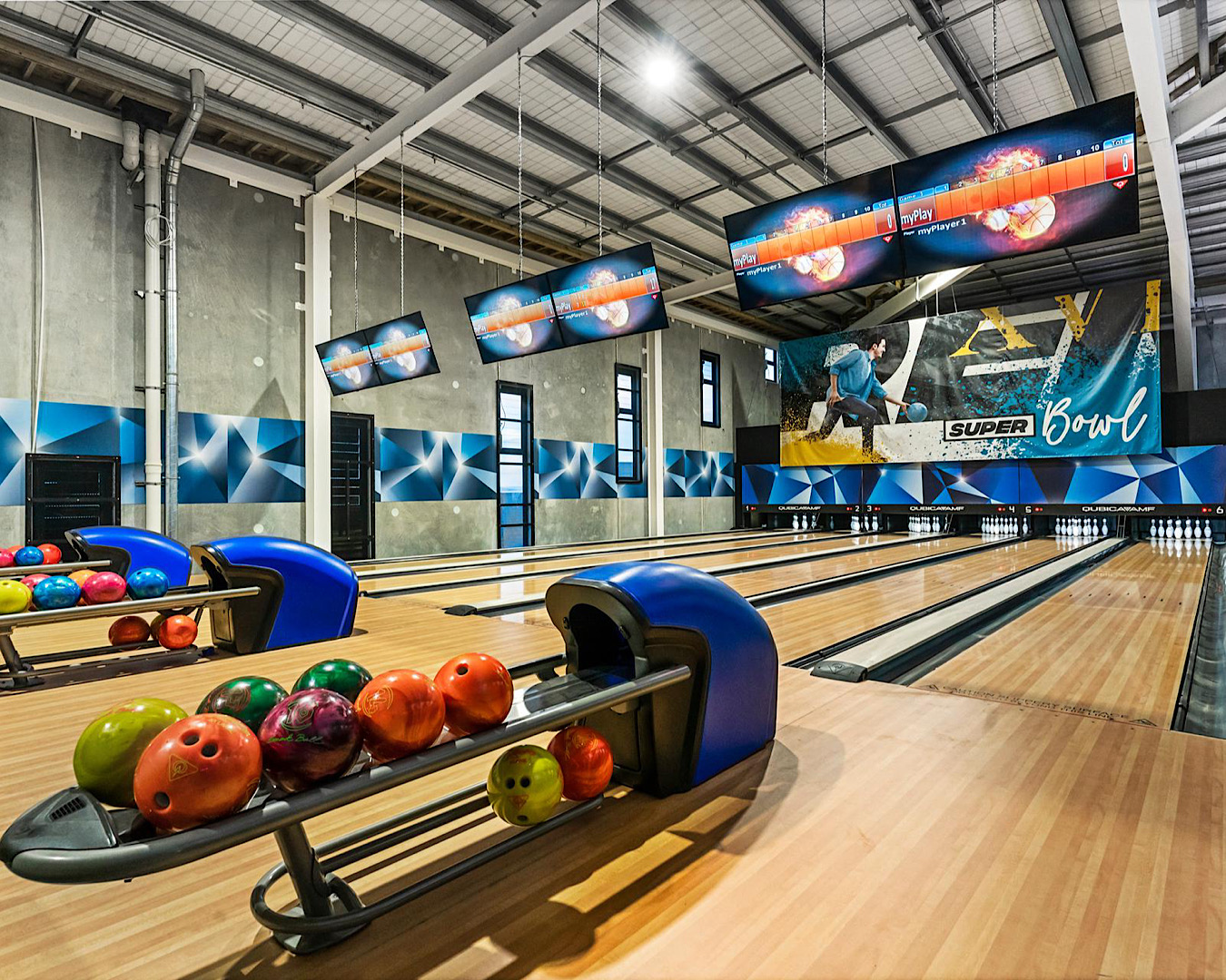 A sleek looking bowling alley with pins lined up in triangles and a bunch of coloured balls waiting on the ball rack. 