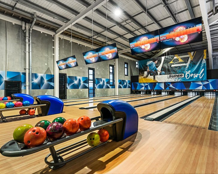 A sleek looking bowling alley with pins lined up in triangles and a bunch of coloured balls waiting on the ball rack. 