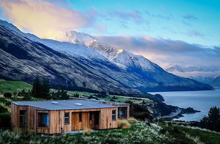 A view of Aro Ha retreat with a cosy looking cabin in the foreground and stunning white-capped mountains behind.