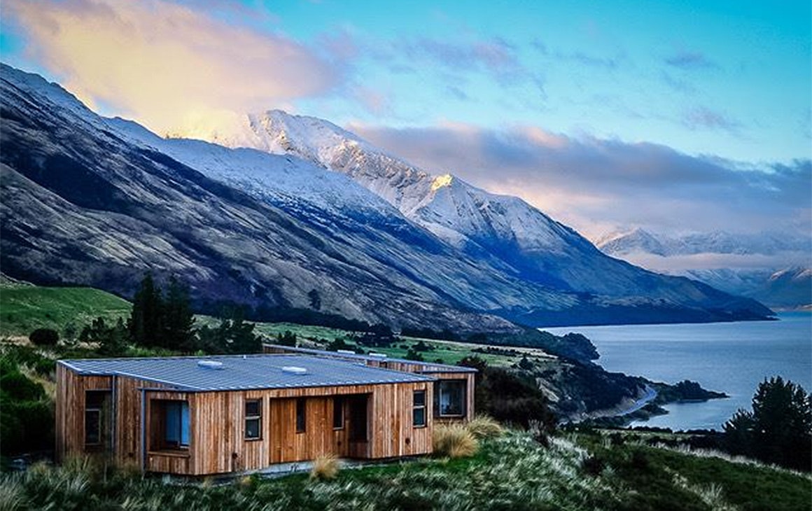 A view of Aro Ha retreat with a cosy looking cabin in the foreground and stunning white-capped mountains behind.