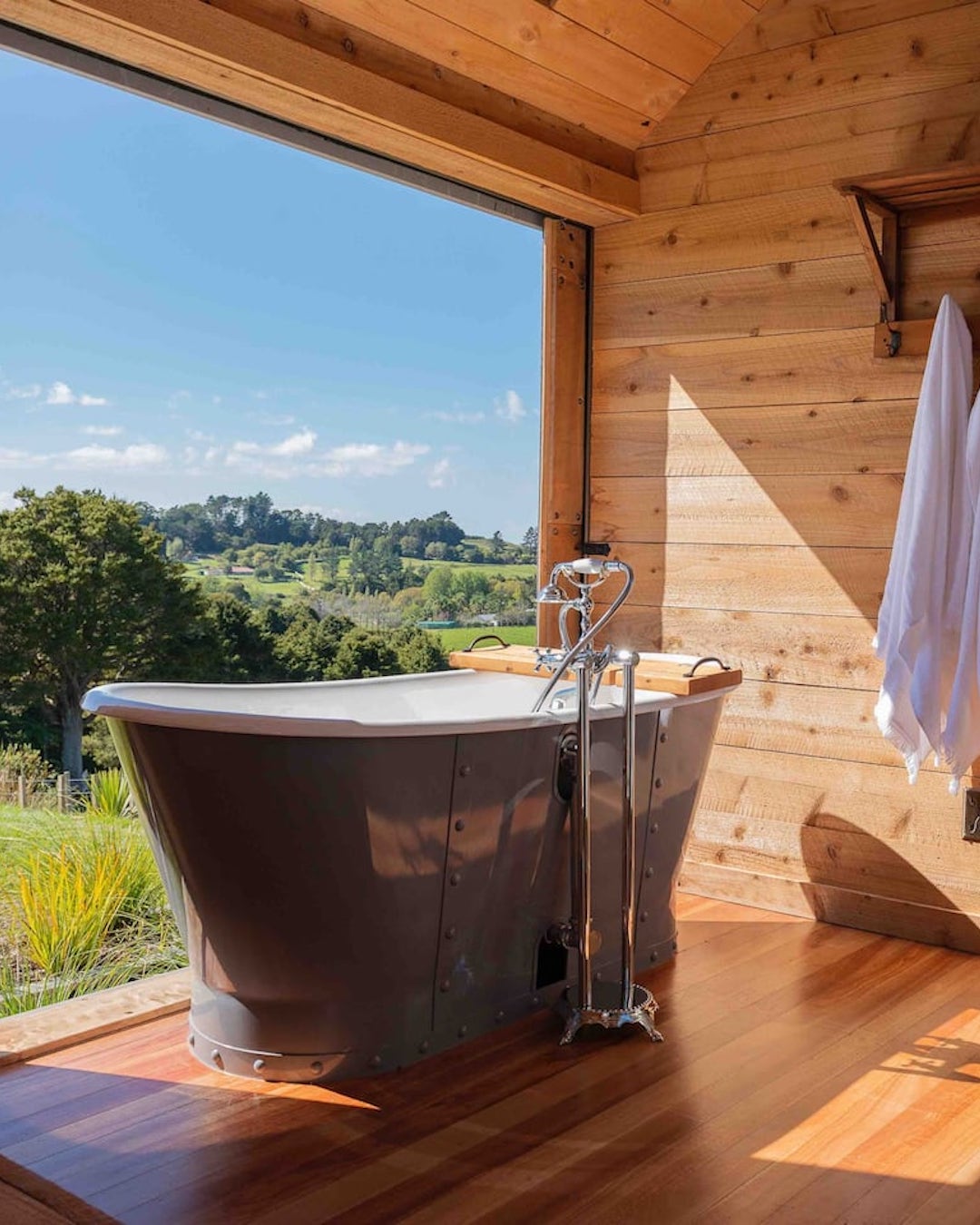 A free-standing bath overlooks green fields, definitely one of the best tiny home airbnbs in NZ.