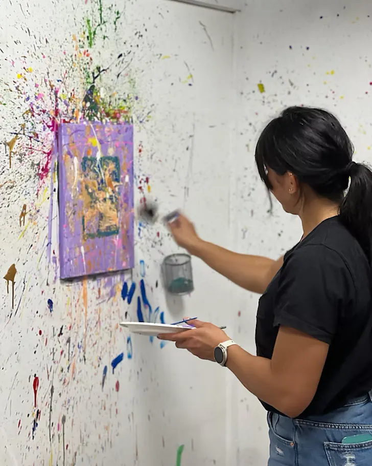 A woman throws a dart at a paint-filled balloon and it explodes. 