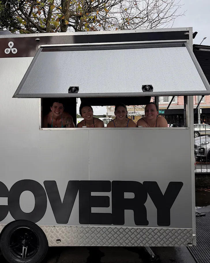 Four happy women look out of a mobile sauna unit.
