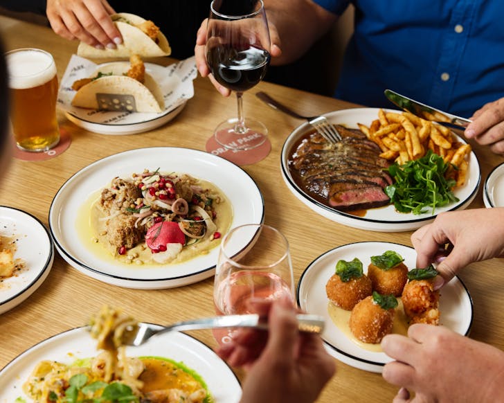A variety of dishes and drinks on a set table along with people sat around eating
