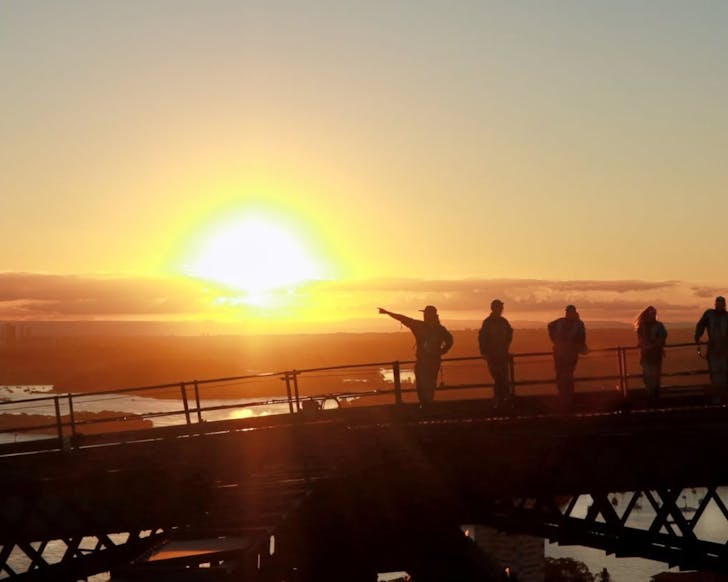 a group of climbers on top of the sydney harbour bridge at sunset
