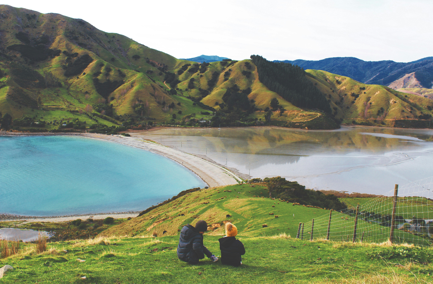 Image of two people sitting on a hill overlooking mountains and lakes in Nelson NZ