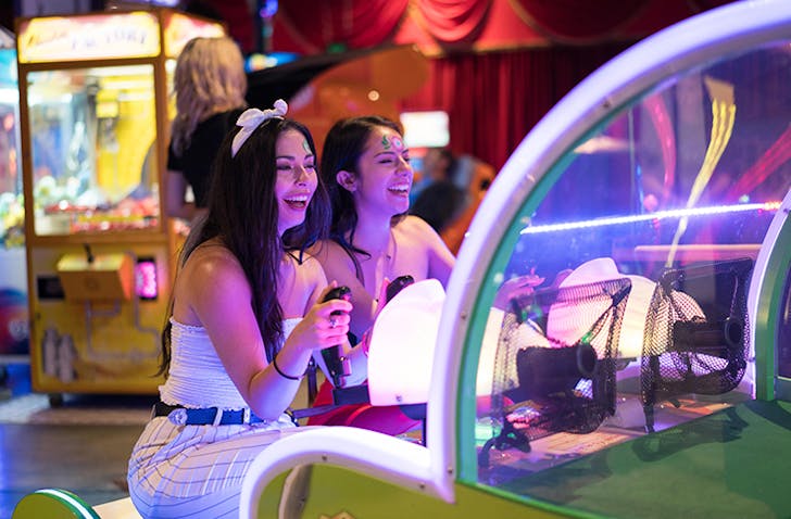 Two women play an arcade game in a colourful circus-themed arcade. 