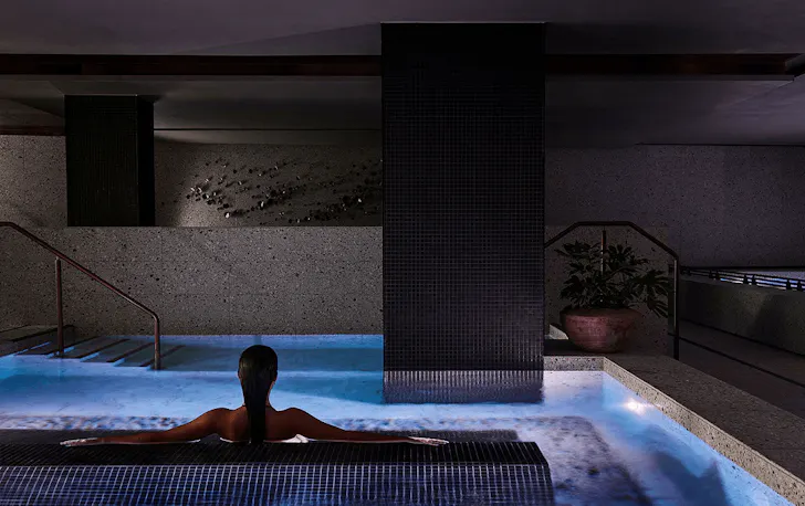 A person sitting inside a spa in a concrete heavy room.