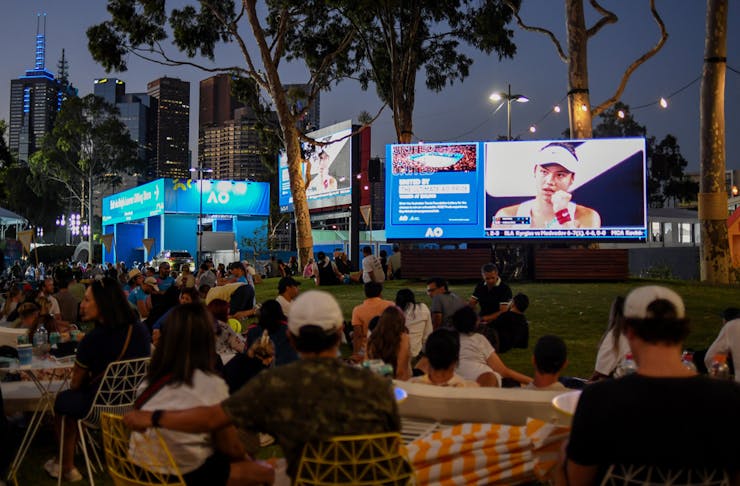 People sitting outside at the Australian Open looking at large screens. 