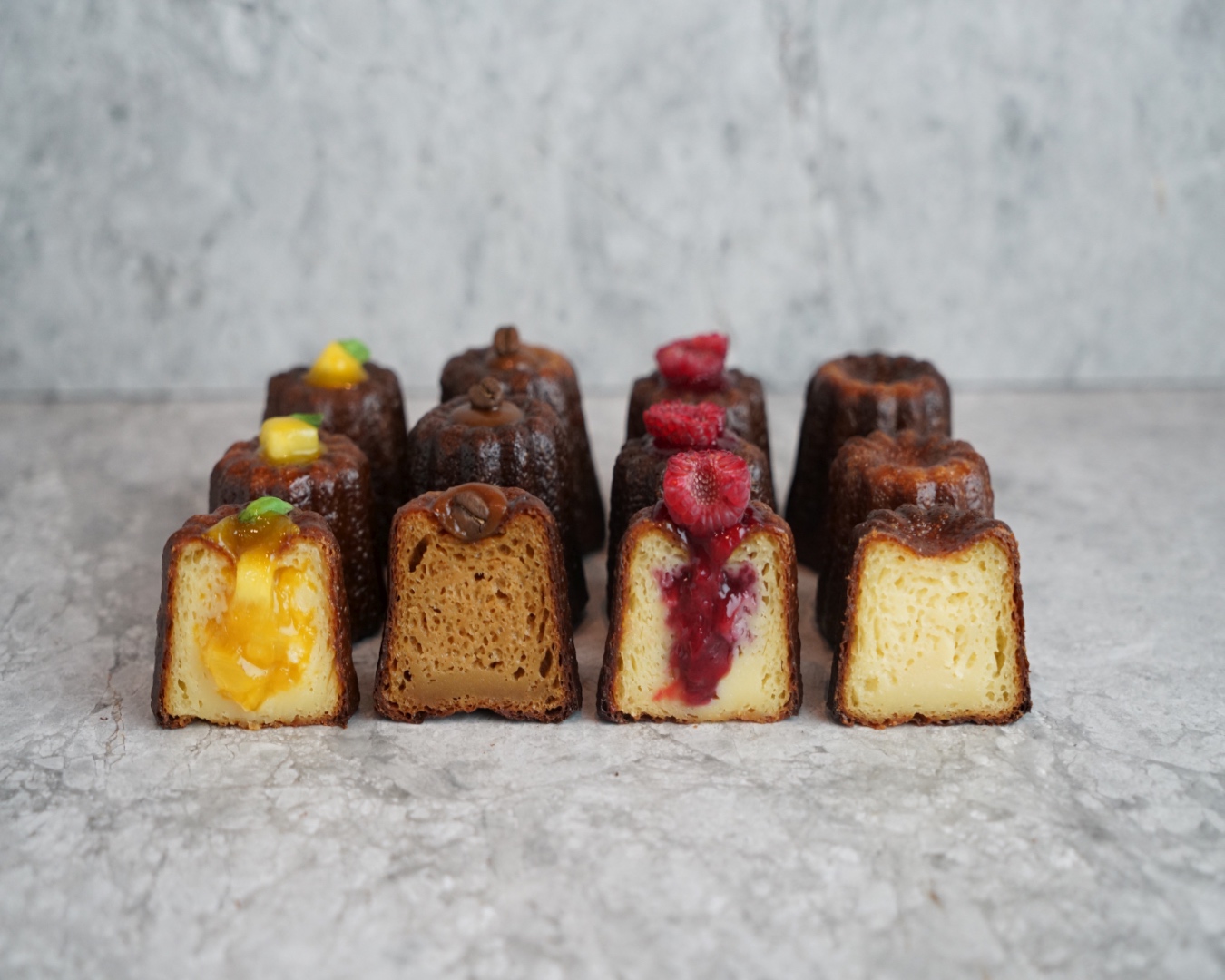 Four cross-sections of canele pastries - lemon curd, raspberry, plain and ginger - on a marble bench