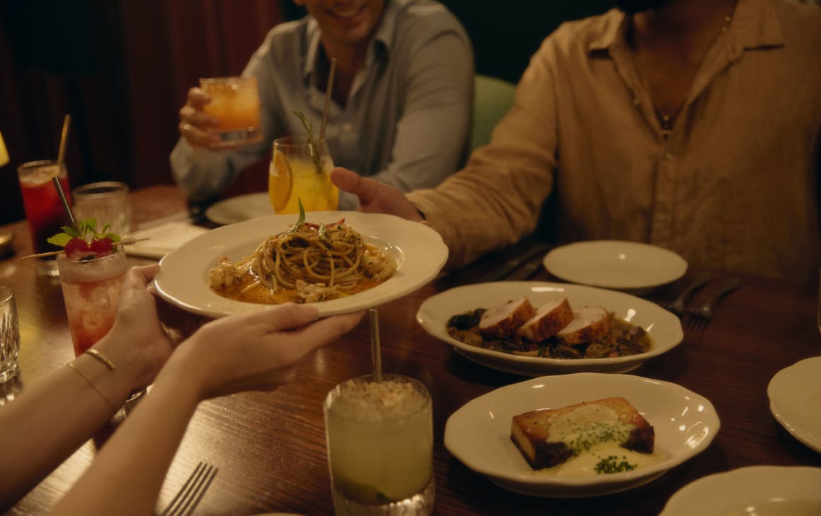 Plate of pasta being passed across table of Italian food and drinks