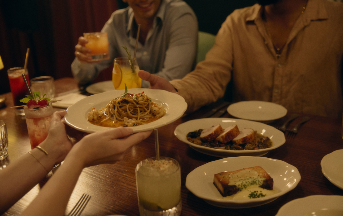 Plate of pasta being passed across table of Italian food and drinks