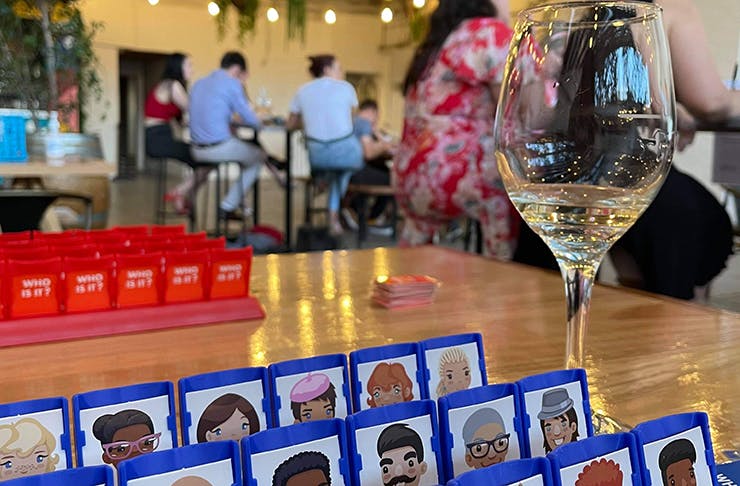 A table of Guess Who with a wine glass next to it 
