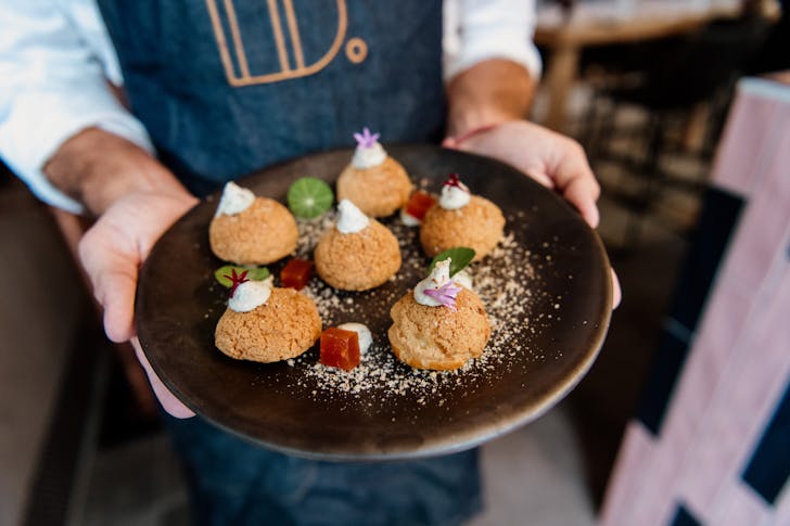 a person with a blue apron holding a dish of savoury profiteroles