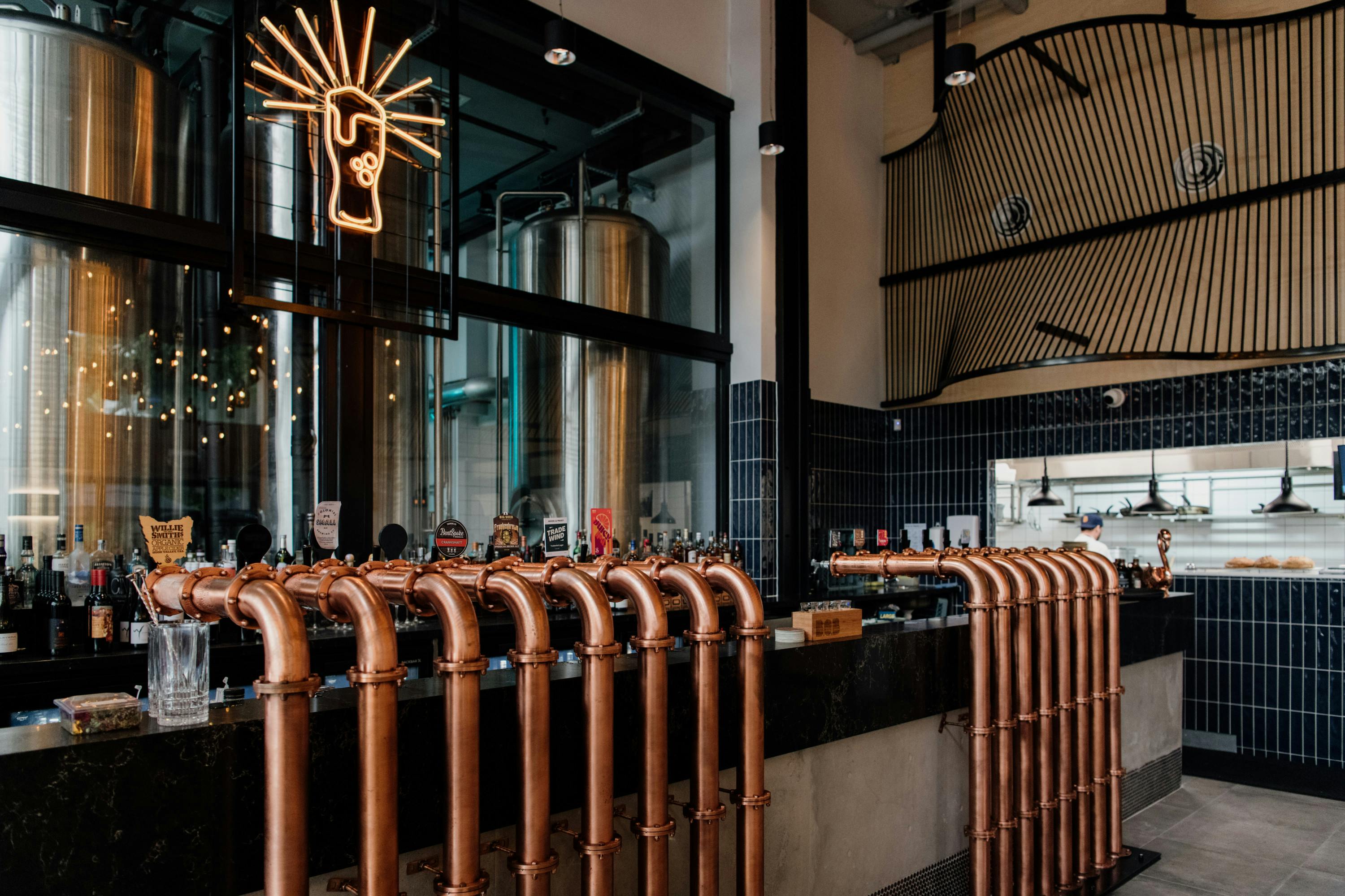 a bar with copper taps and a beer glass neon hanging above it
