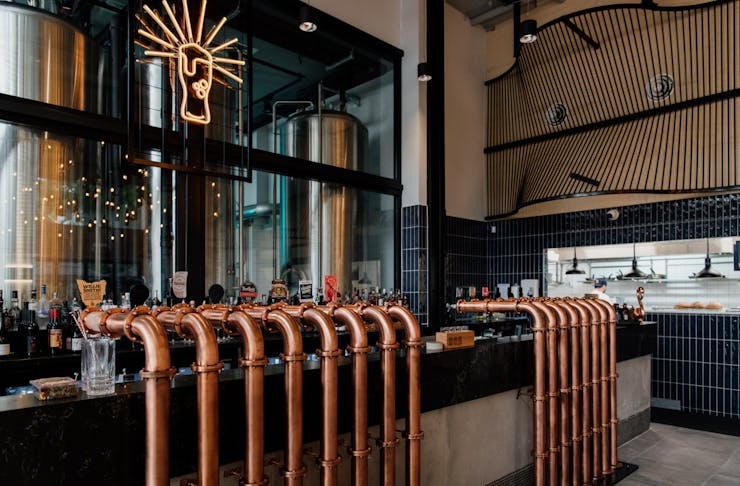a bar with copper taps and a beer glass neon hanging above it