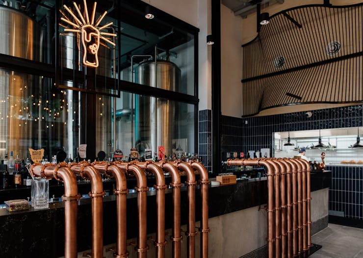 a bar with copper taps and a beer glass neon hanging above it