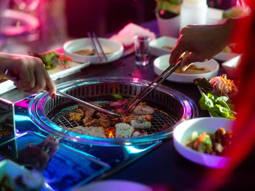 A Korean BBQ table with pink and blue neon lights. 