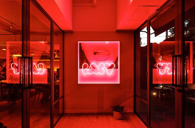 The entrance to Baby Pizza with red neon lights and artwork. 