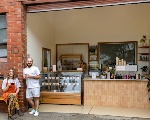 Two people smiling at the front of a bakery. 
