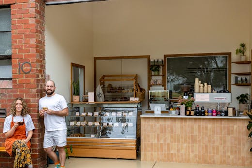 Two people smiling at the front of a bakery.