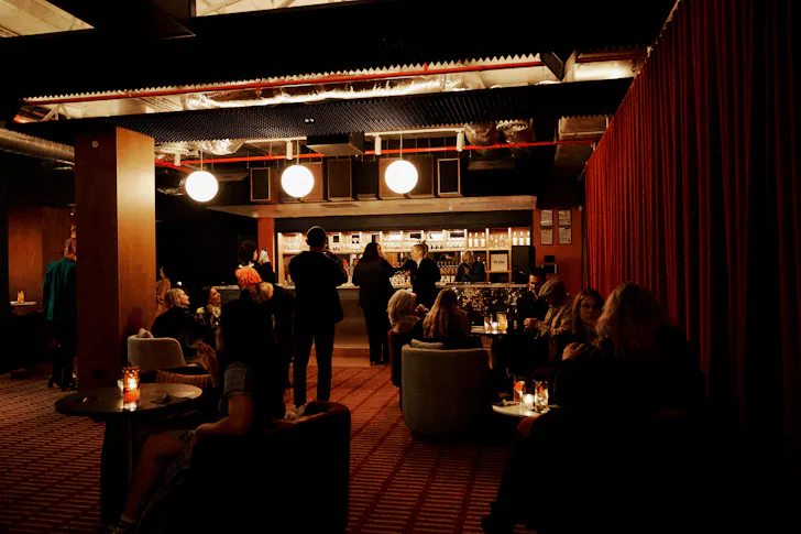 The inside of a bar with people drinking and a lit up standing area.