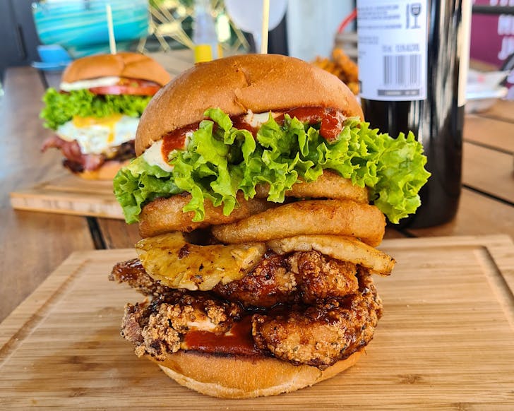 An absolutely stacked, saucy burger with hashbrowns, pineapple, lettuce, sauce, and crispy chicken.