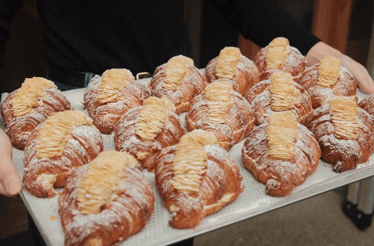 A person holding a tray of baked almond croissants.