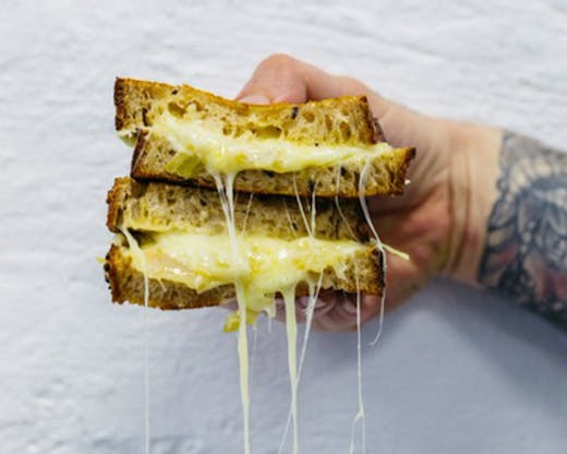 A sandwich being held up with cheese oozing out.