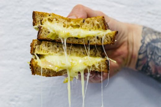 A sandwich being held up with cheese oozing out.